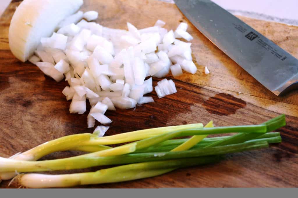 Green onion and diced white onion on a cutting board.