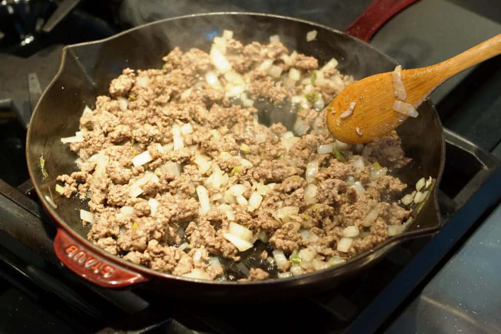 Ground beef and onion cooking in a cast Staub skillet.