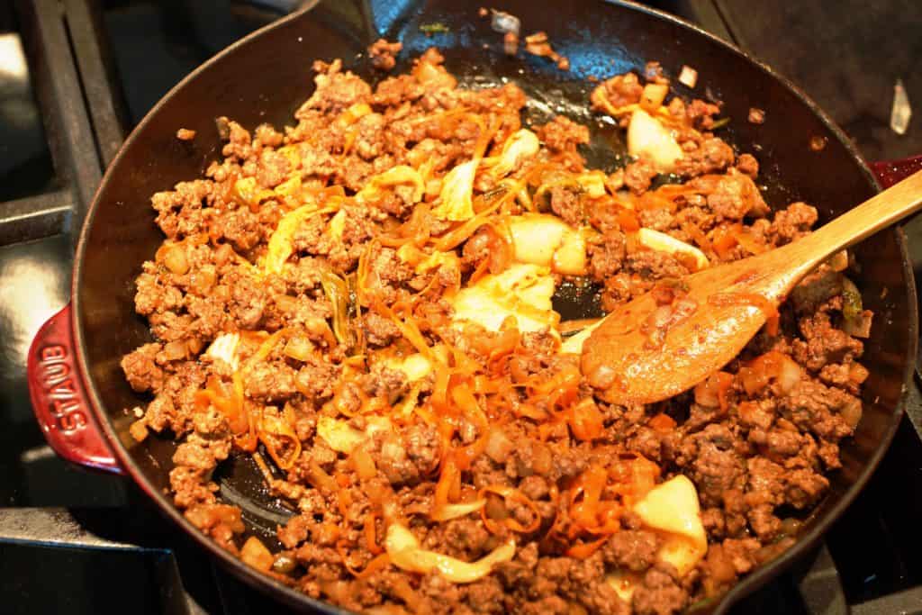 Kimchi being stirring into seasoned beef.