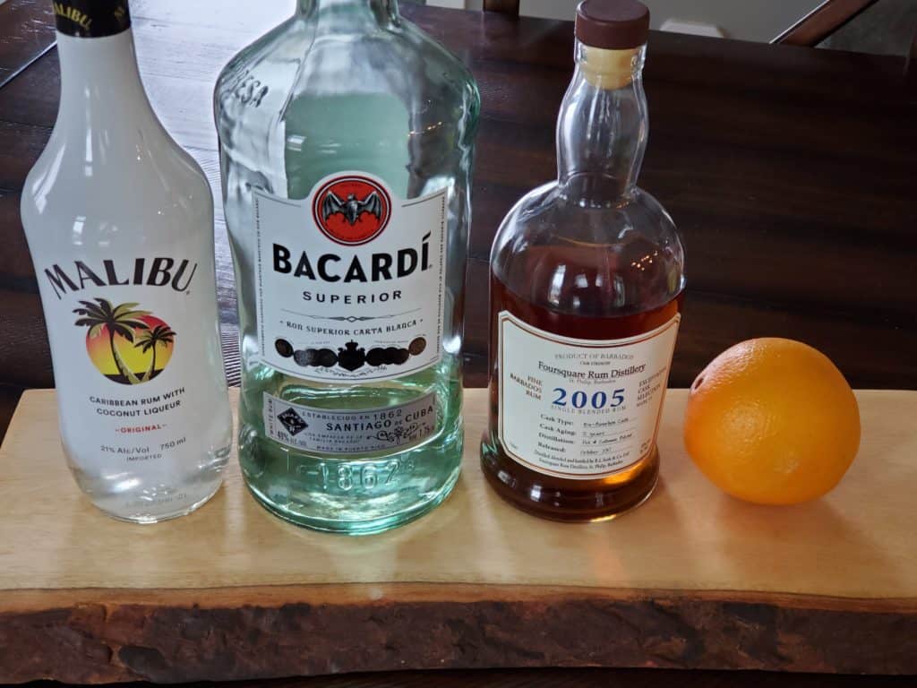 Coconut rum, white rum, and dark rum on a table with an orange.