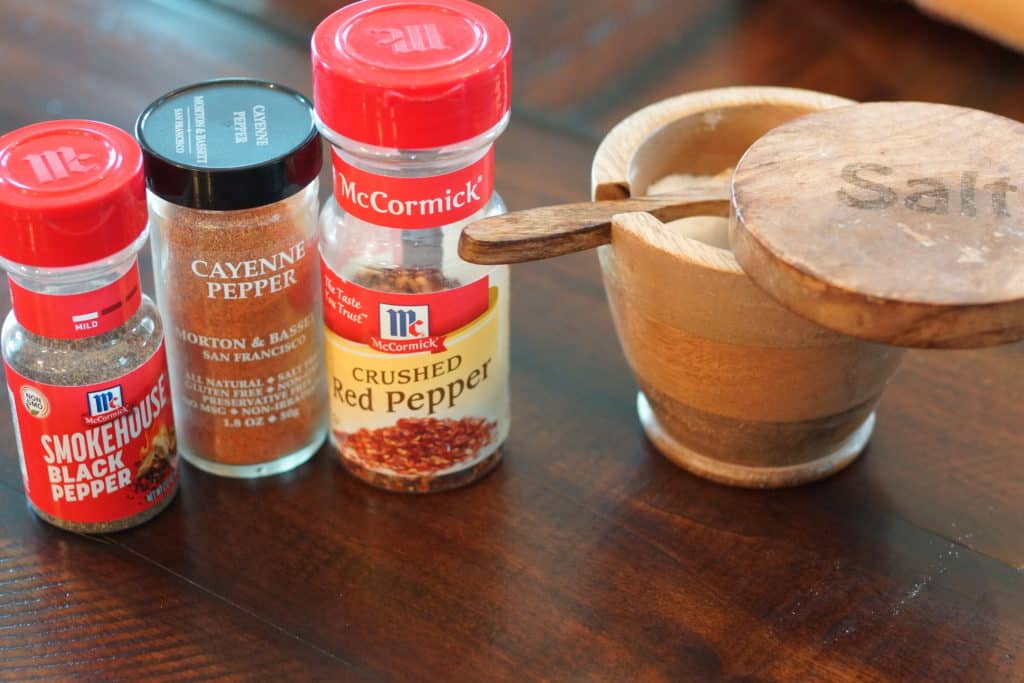 Salt, cayenne, crushed red pepper, and black pepper on a cutting board.