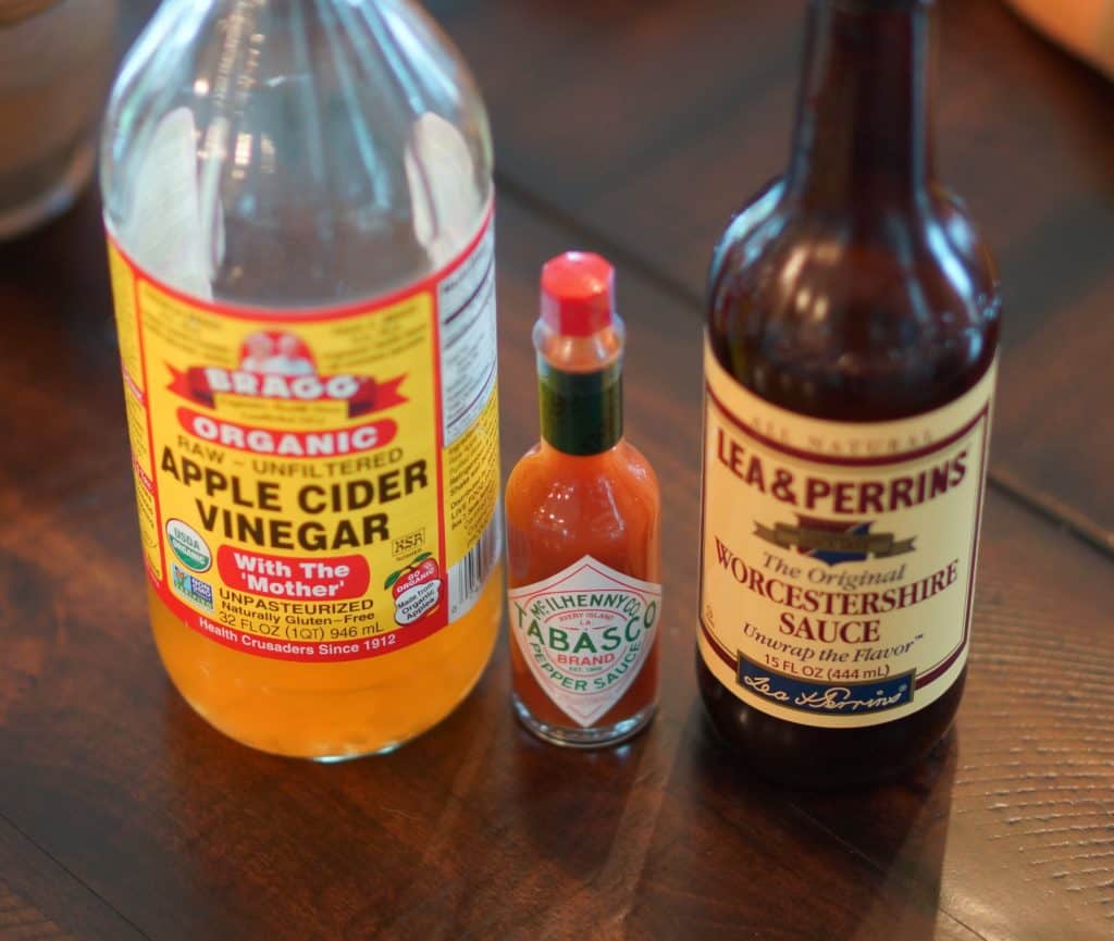 apple cider vinegar, tabasco, and Worcestershire sauce on a wood table.