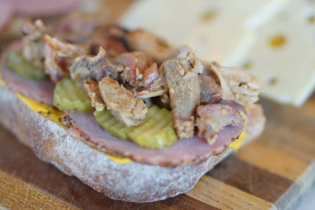 Roasted pork in a sandwich with pickles and ham.