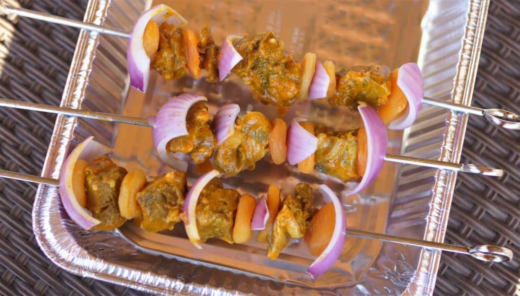 Metal skewers with lamb, red onion, and dried apricots.
