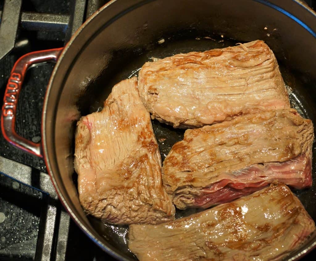 Flank steak browning in a Dutch oven.