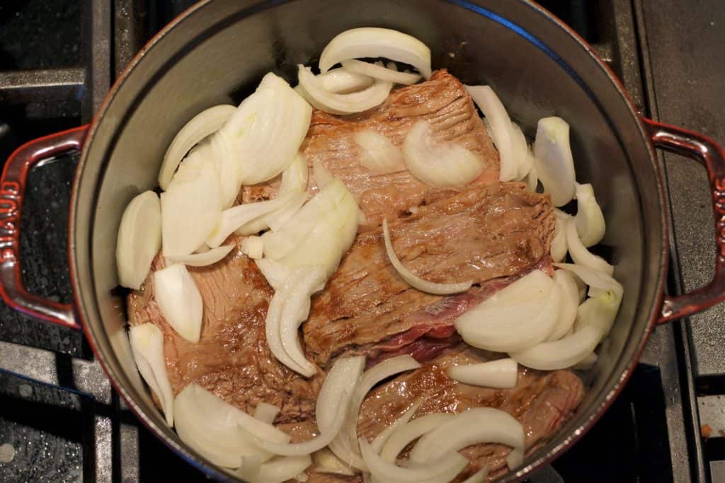 Onion added to a Dutch oven with flank steak.