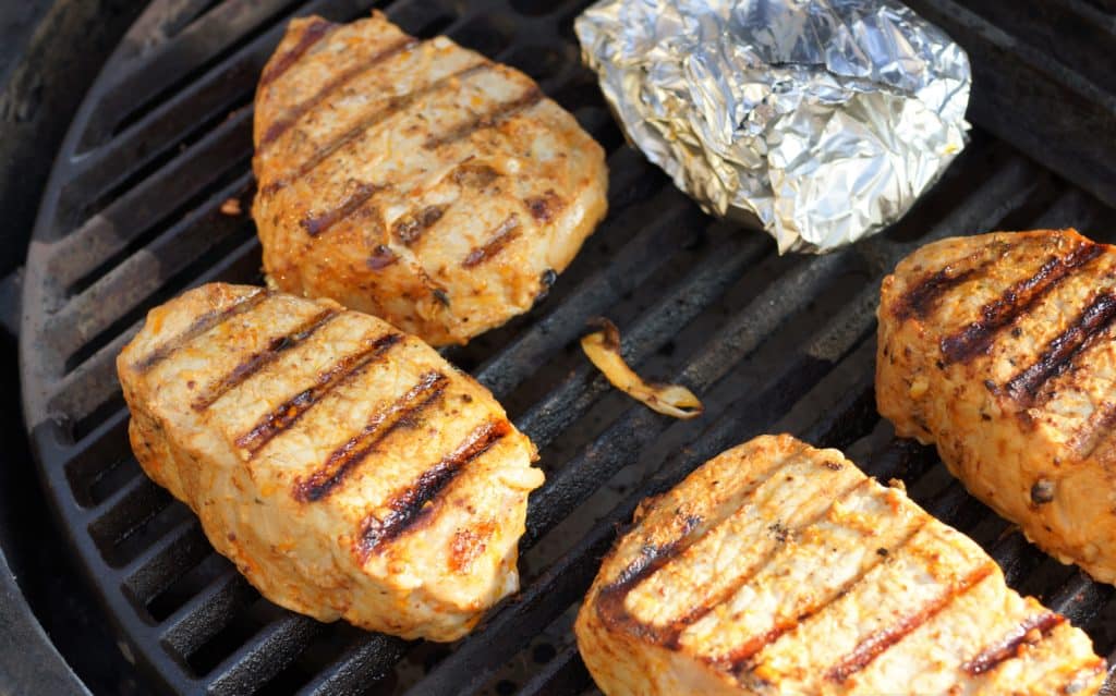 Pork chops cooking on a grill.