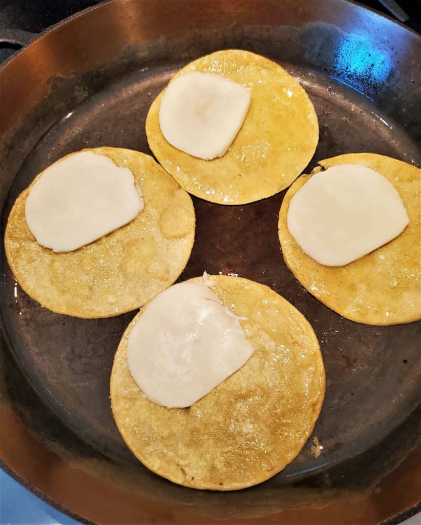 Corn tortillas topped with mozzarella slices in a frying pan.