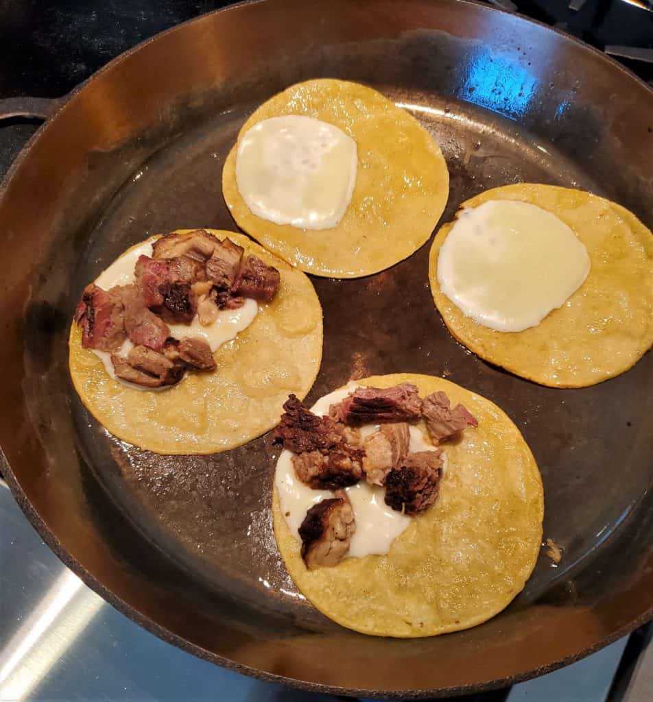 4 corn tortillas in a frying pan.  2 topped with mozzarella and 2 topped with cheese and brisket.