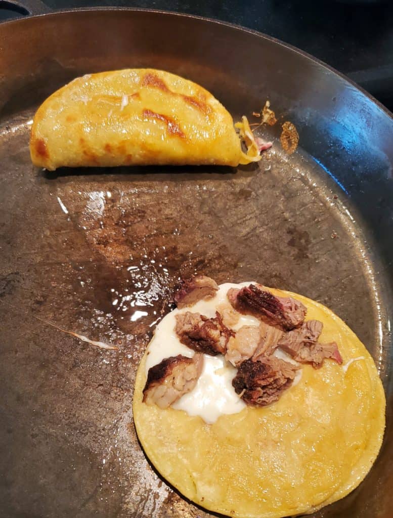 Corn tortilla tacos with cheese and brisket frying in a pan.