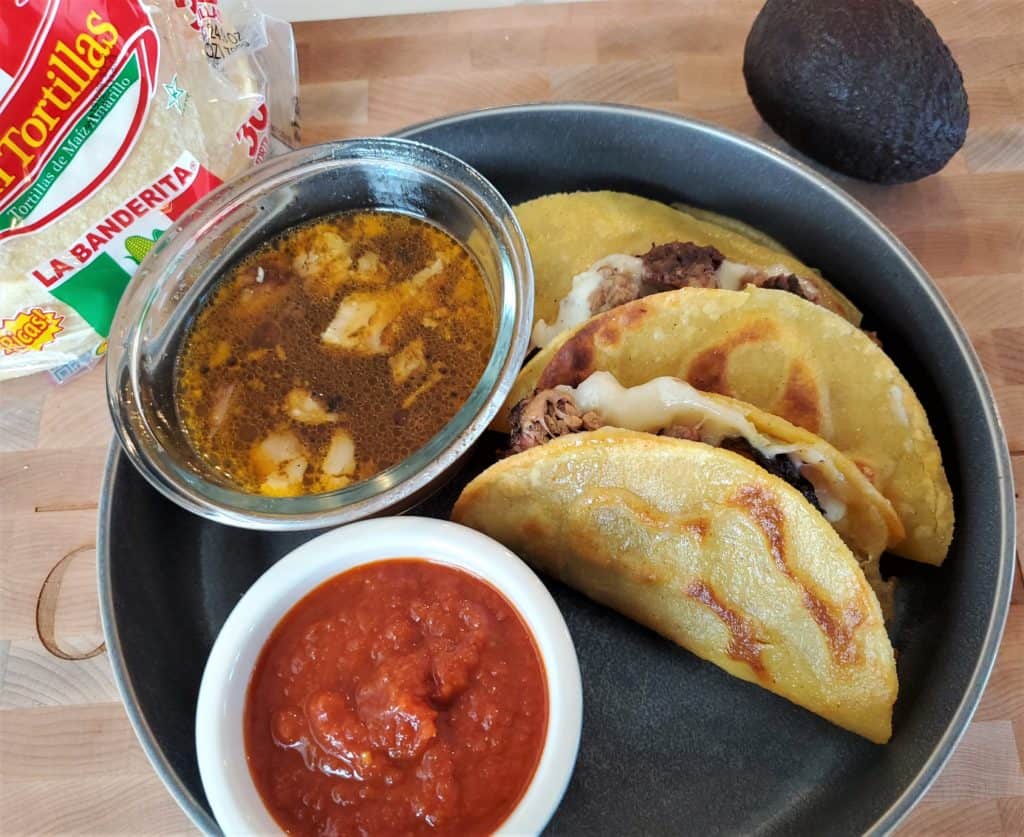 Plate of brisket quesabirria tacos served with consommé and salsa.