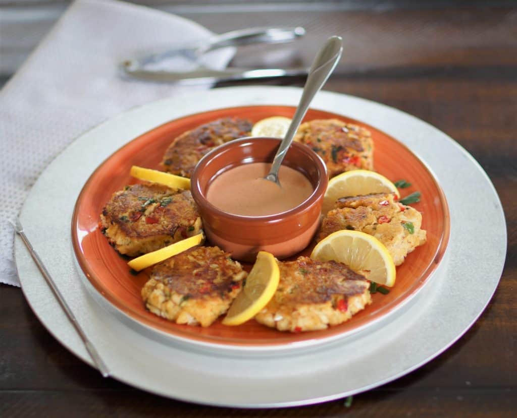 Fried crab cakes and lemon slices arranged on a plate around a cup of Sriracha Aioli