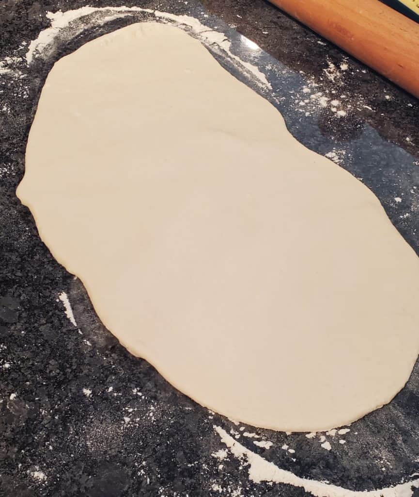 Pizza dough rolled out on a floured counter into an oblong shape.