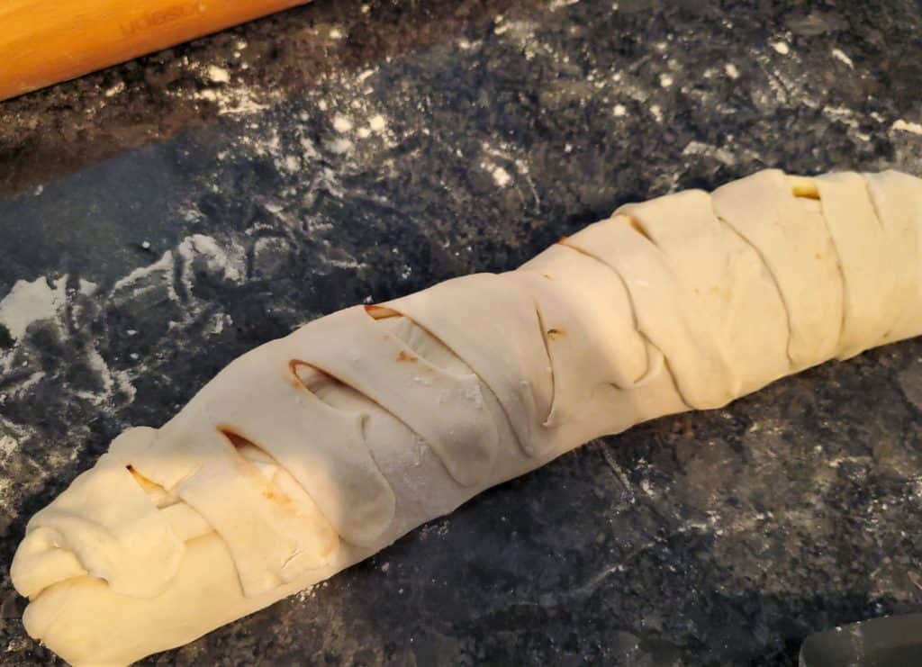 Stromboli shown rolled up on a floured counter.