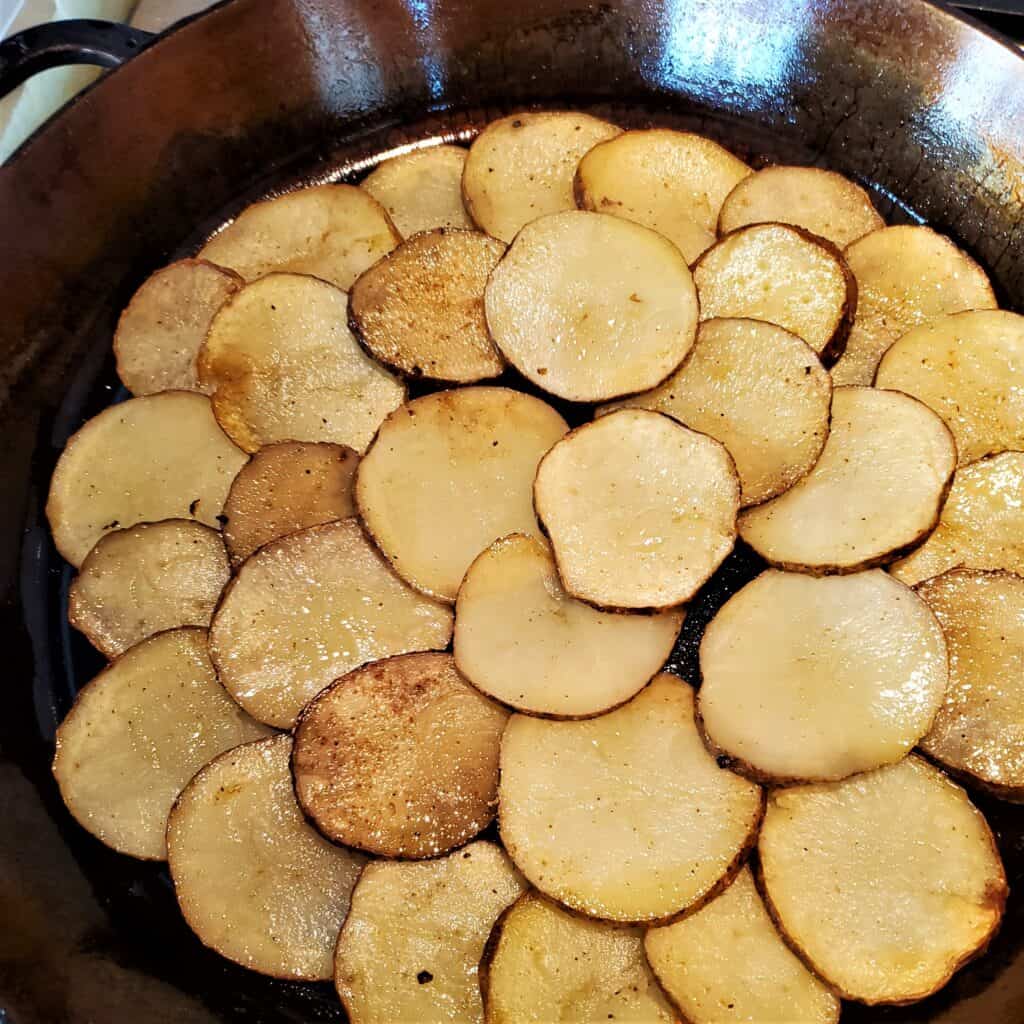 Fried potatoes arranged in a layer in a cast iron pan.