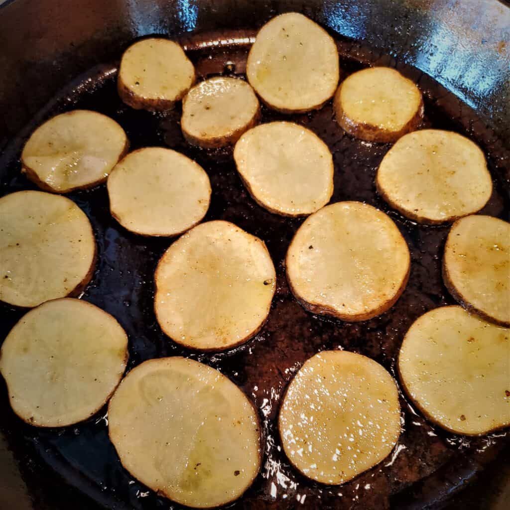 Russet potato slices frying in a cast iron pan.