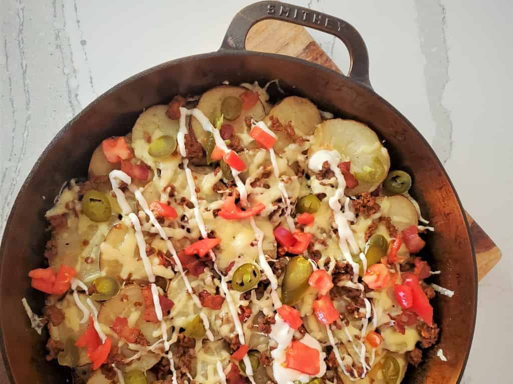 Pub Style Irish nachos in a Smithey cast iron pan.  Topped with taco meat, tomatoes, melted cheese, jalapenos, and sour cream.