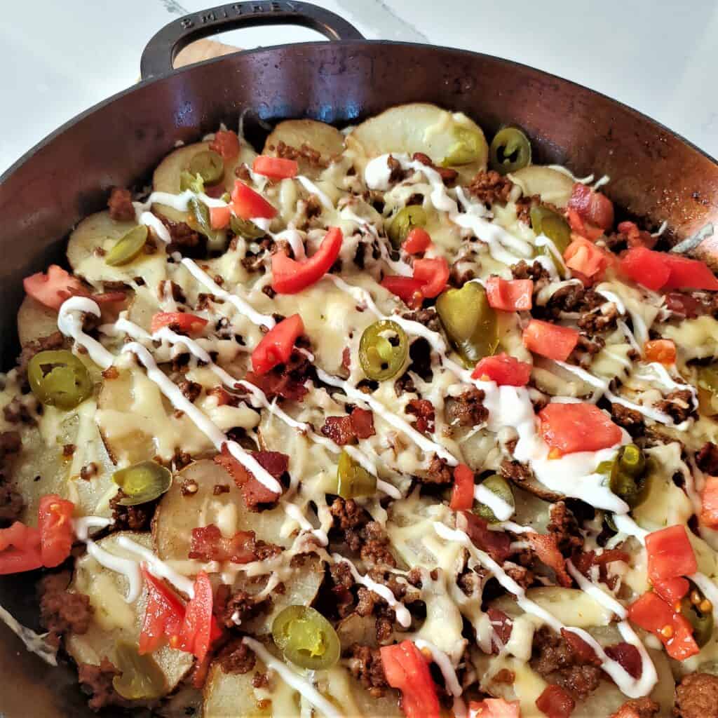 Irish nachos with taco meat, jalapenos, tomatoes, melted cheese and sour cream in a cast iron pan.