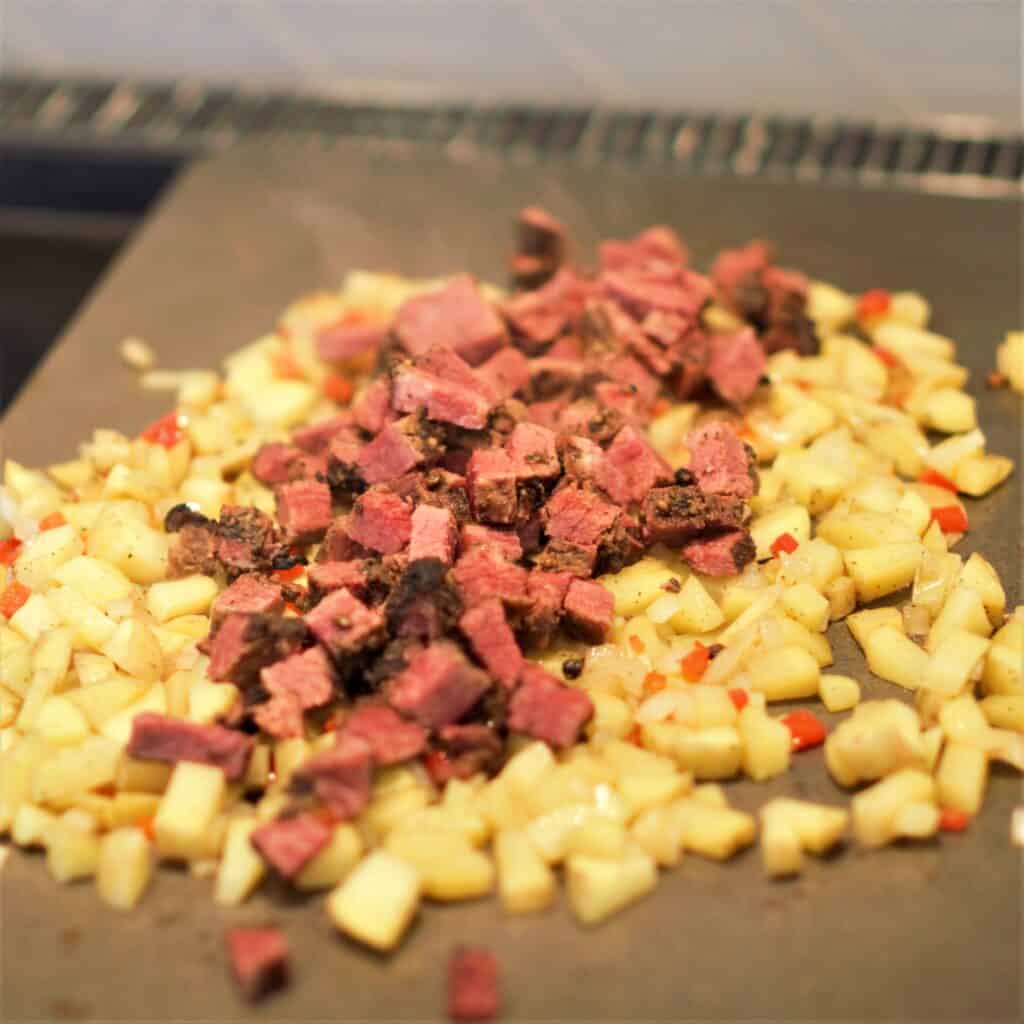 Pastrami hash cooking on a Cooking Steel on a stove top.