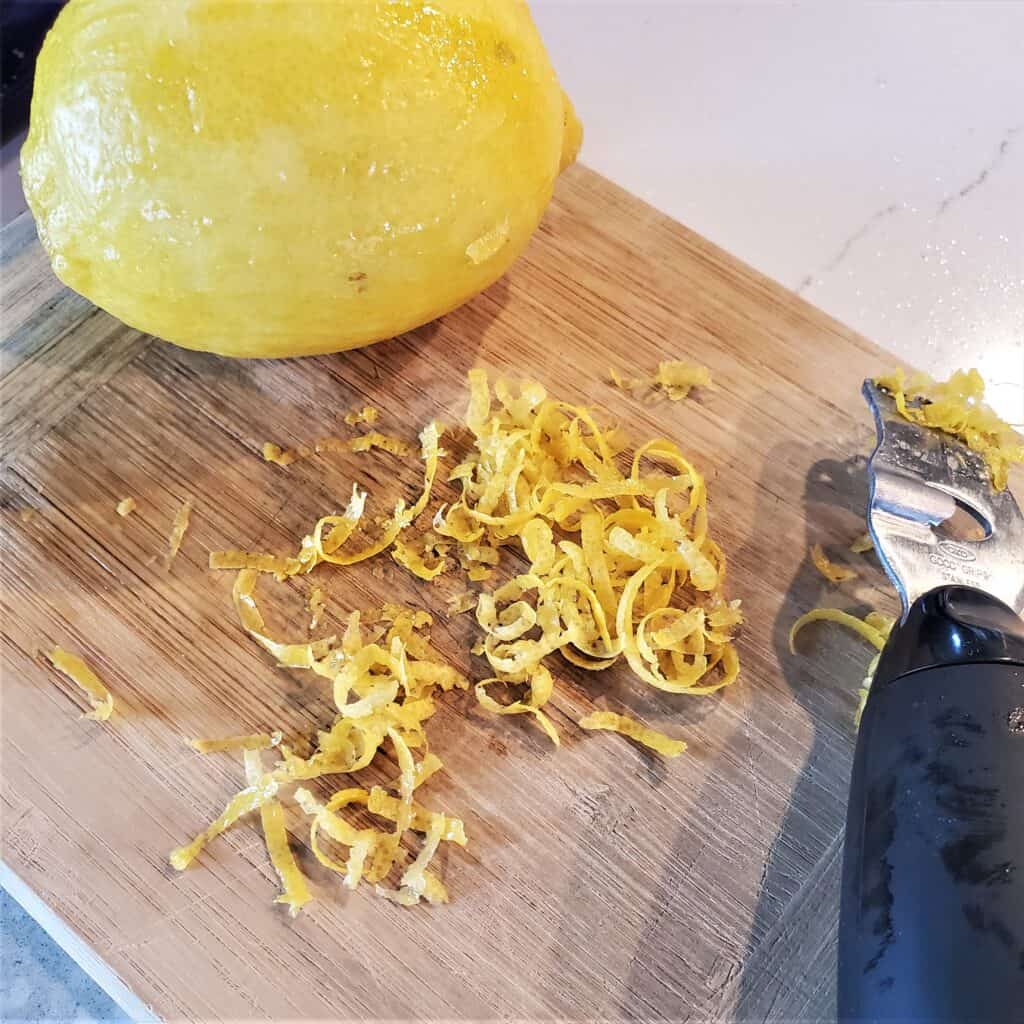 Lemon being zested on a small cutting board
