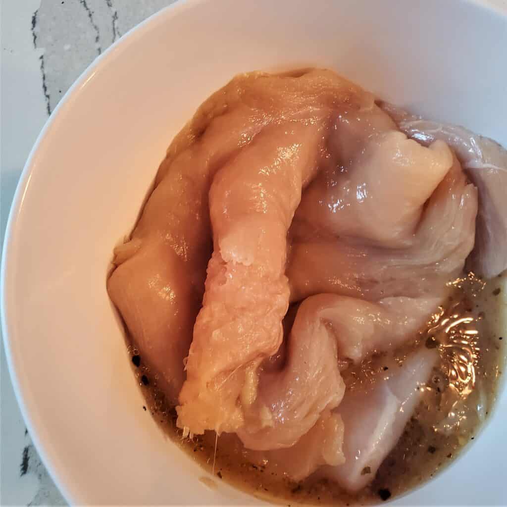 Chicken breasts in a bowl of amogio marinade.