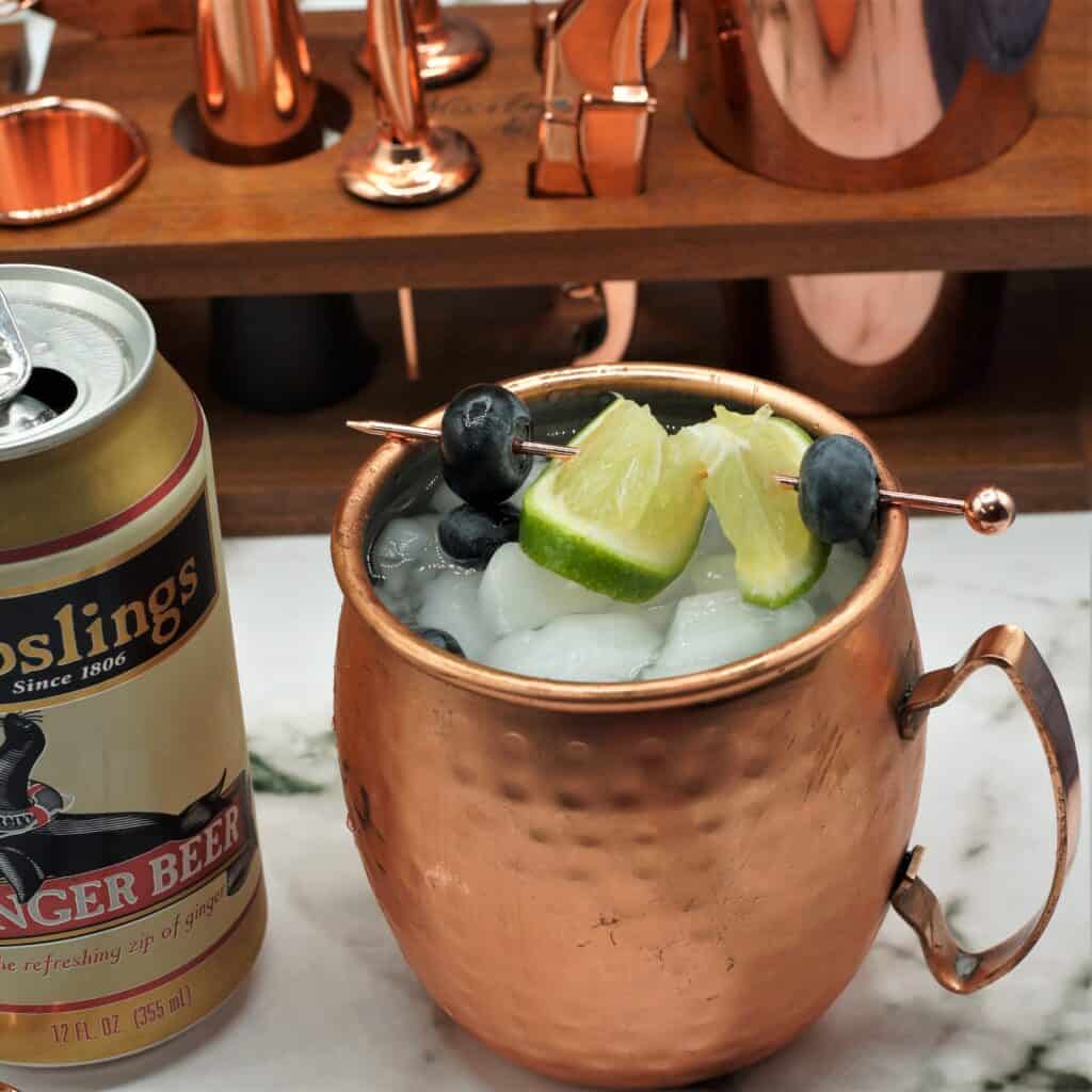 Copper mug of blueberry Moscow mule next to a can of ginger beer.