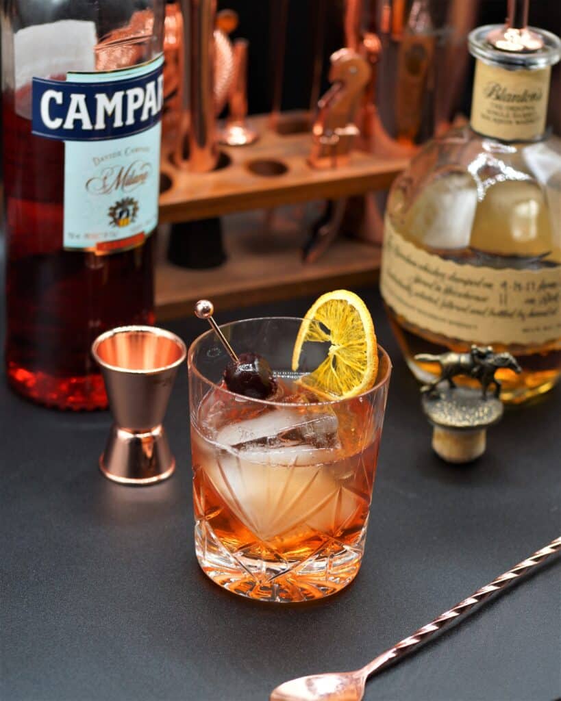 Tumbler with a Campari Old Fashioned next to bottles of Campari and Blanton's Bourbon