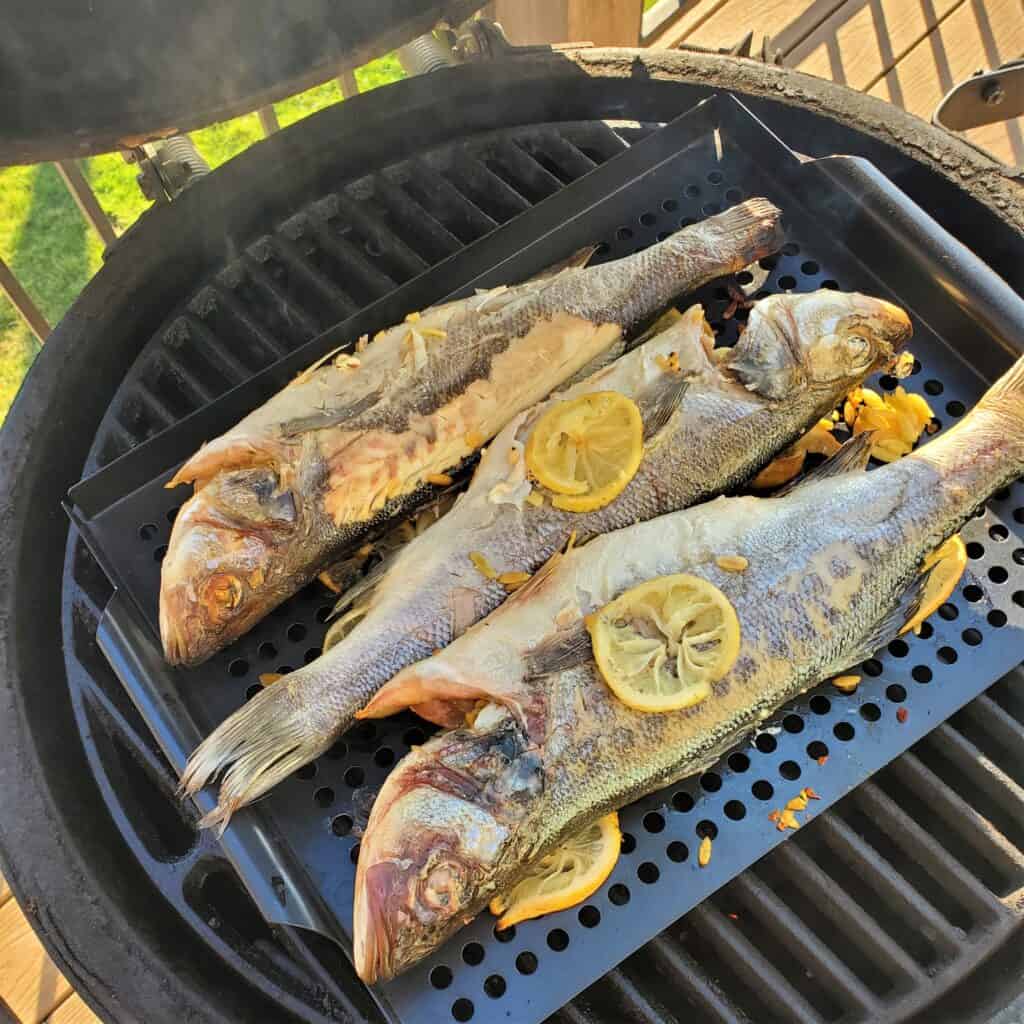 3 grilled branzino, stuffed with orzo and feta, on a grill.