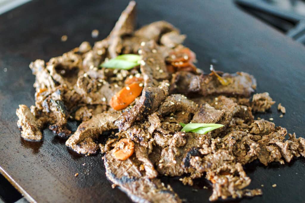 Beef bulgogi cooking on a flat top grill