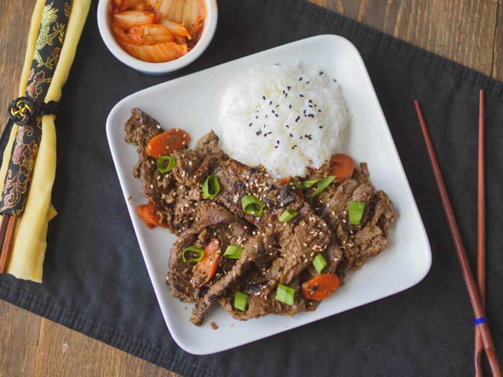  A square white plate with beef bulgogi and white rice and a side of kimchi.