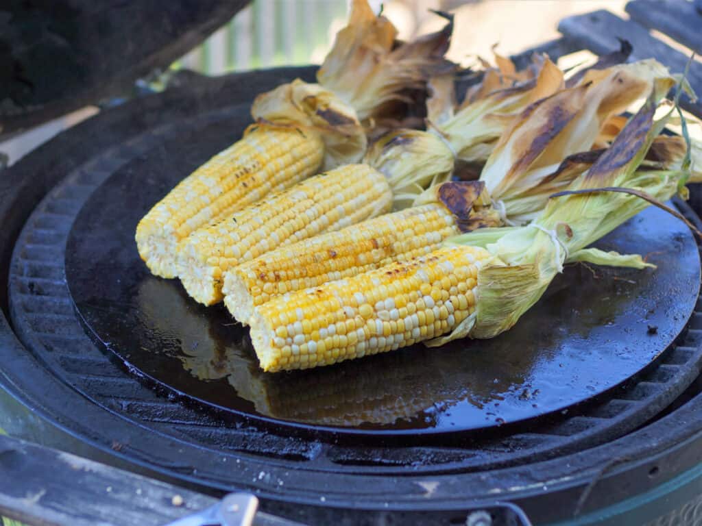 4 Corn cobs roasting on a griddle.