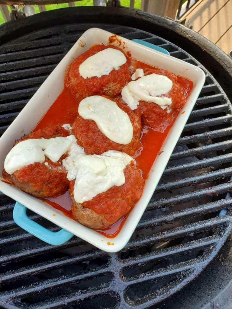 Pan of 5 meatballs topped with burrata on a BBQ grill.