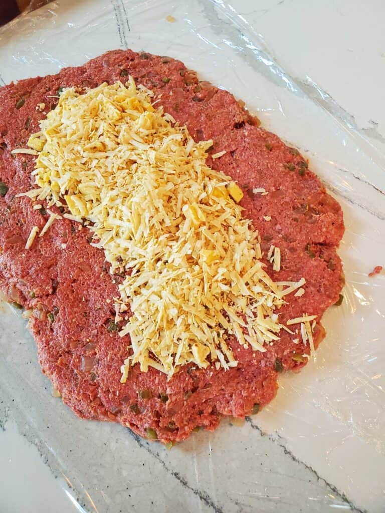 Shredded cheese on top of ground beef, ready to be formed into a stuffed meatloaf.