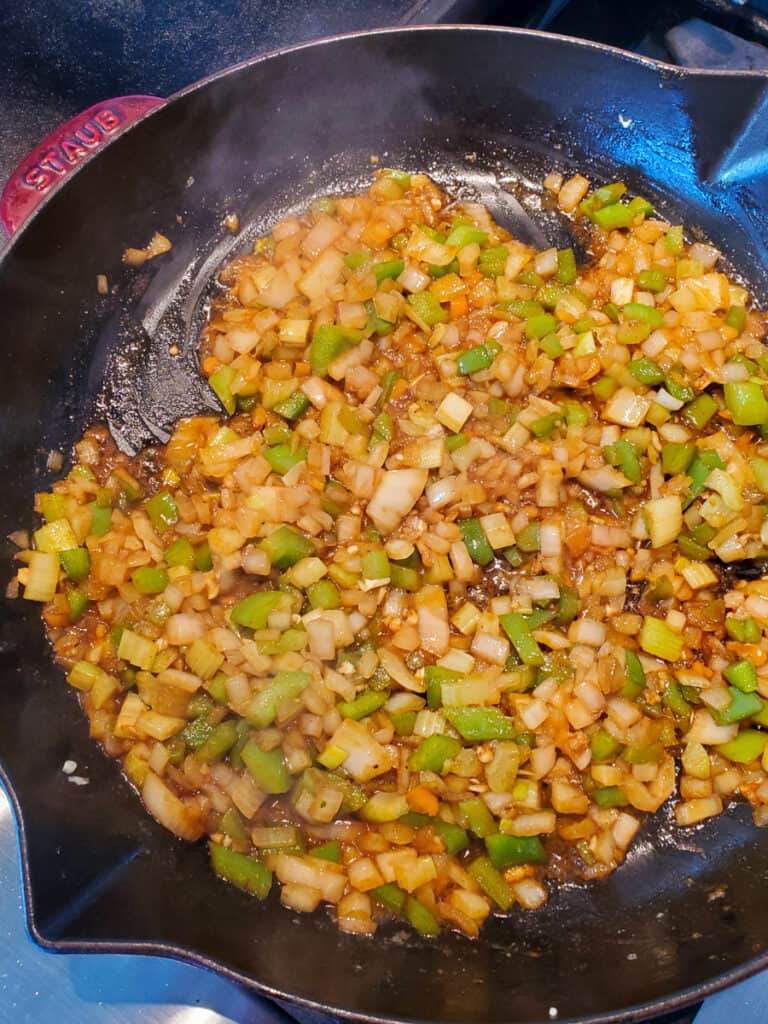 Sautéed onions, celery, and bell pepper in a cast iron pan with spices and seasoning.