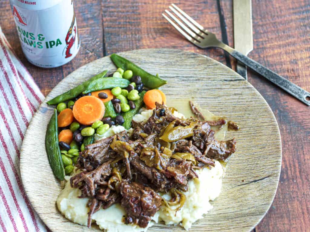 Plate of smoked Mississippi Pot Roast served over mashed potatoes with vegetables.