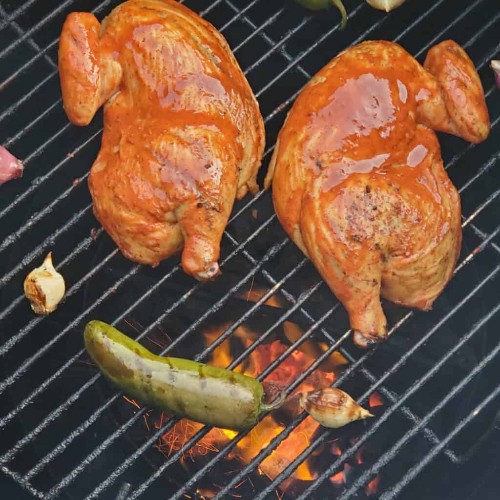 Two chipotle chicken halves grilling on a Gateway Drum smoker.