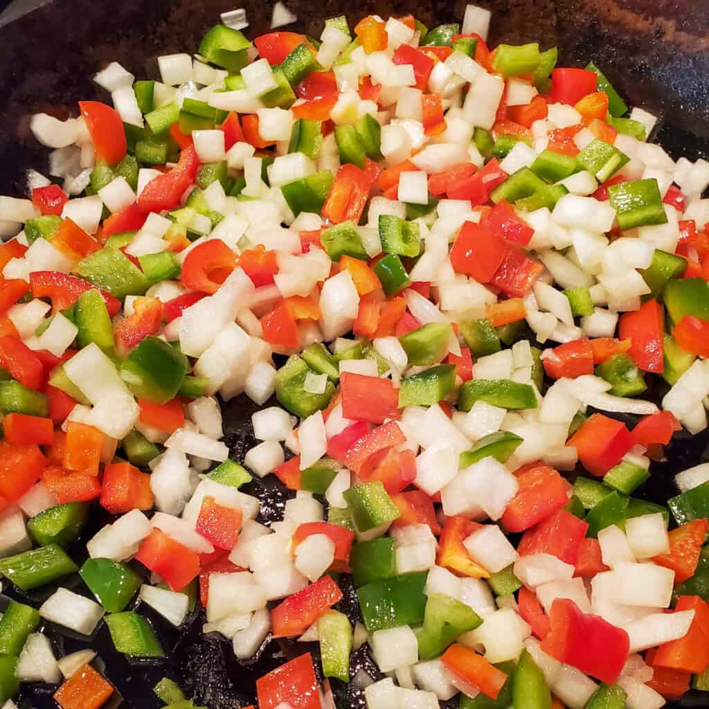 Diced onion and peppers sauteing in a pan.