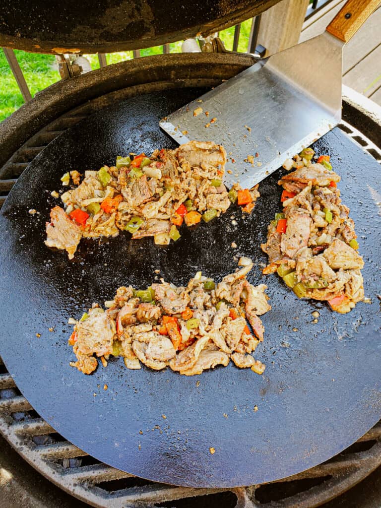 Philly cheesesteak meat being cooked on a Cooking Steel griddle on a Big Green Egg.