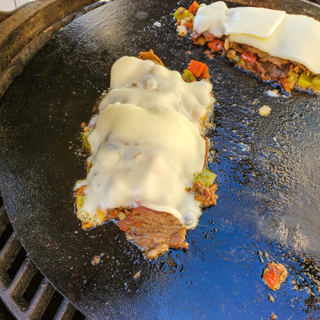 Philly cheesesteak cooking on a griddle.
