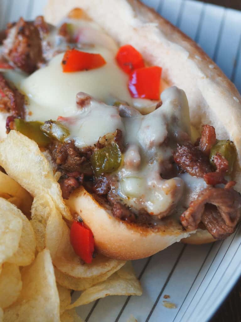 Smoked Philly Cheesesteak on a hoagie roll, with chips.