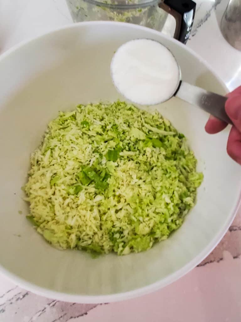 Salt and sugar being added to shredded cabbage.