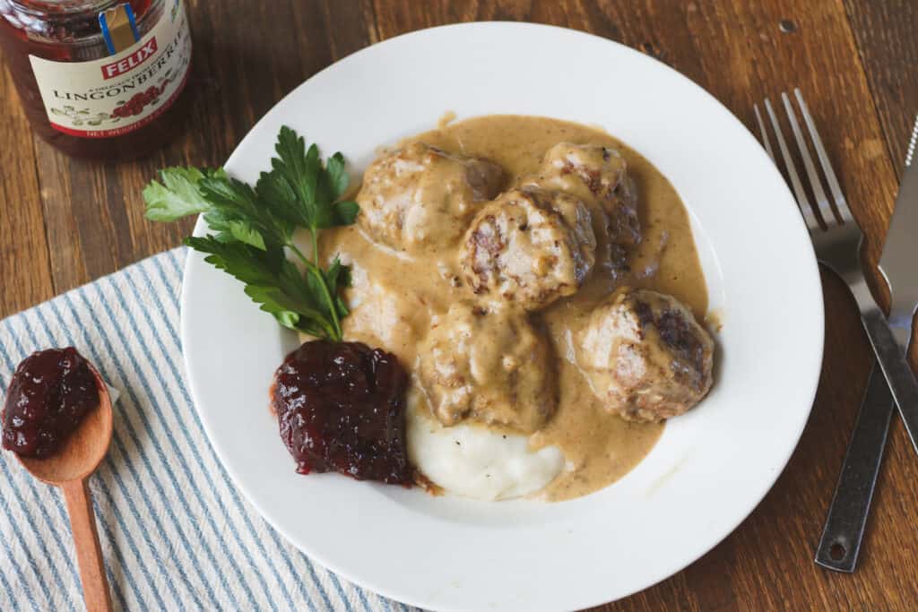 White plate with Sedish meatballs over mashed potatoes with lingonberries.