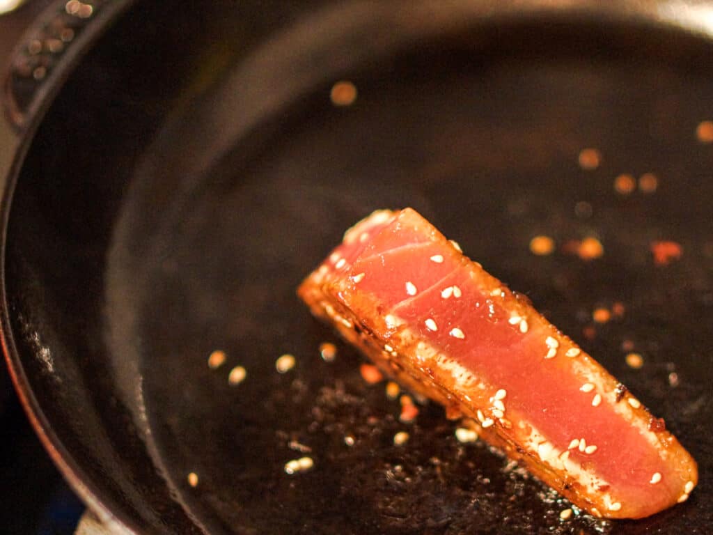 Ahi tuna steak searing in a cast iron pan.