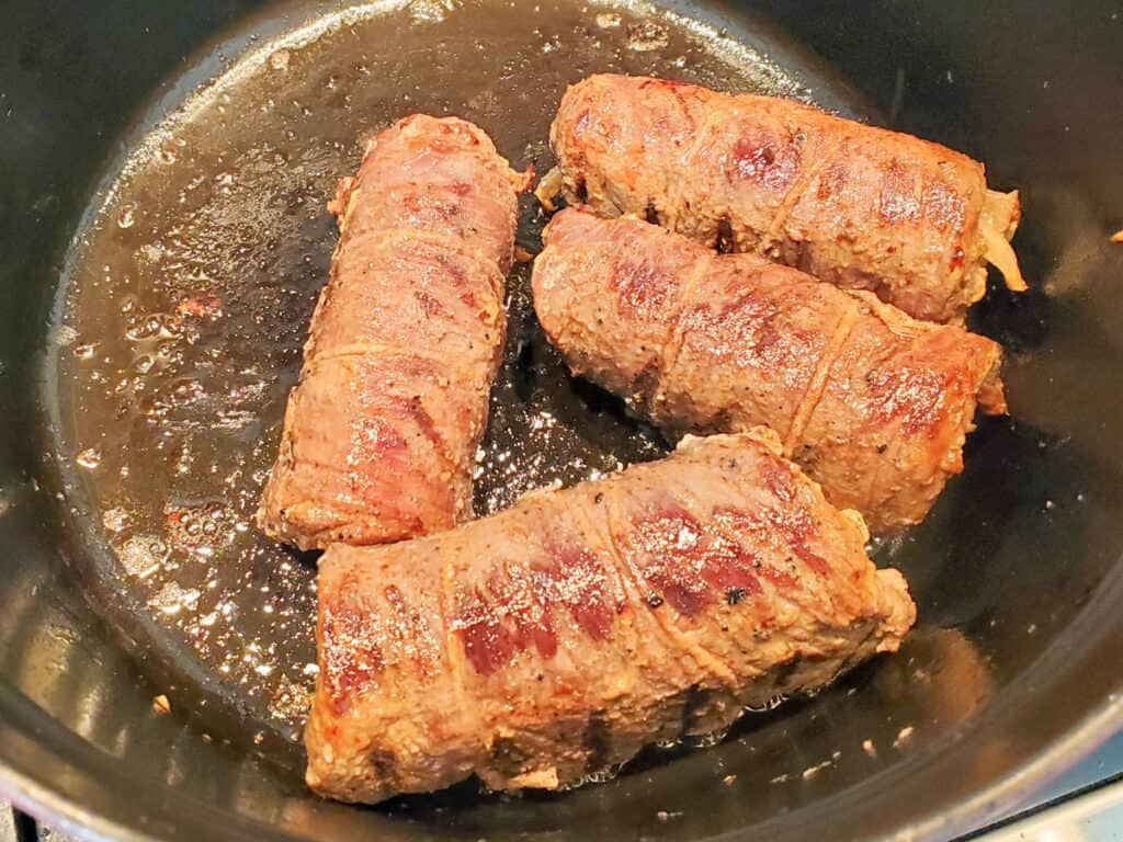 Rouladen cooking in a cast iron pan.
