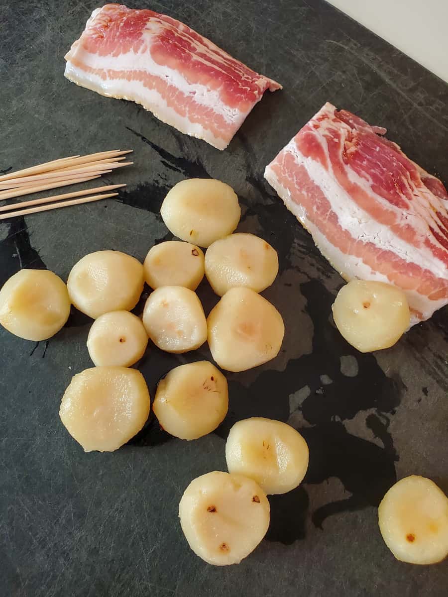 Water chestnuts and bacon on a black cutting board.