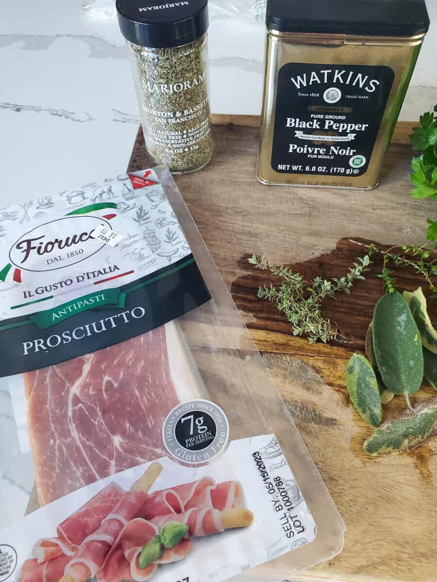 Prosciutto, black pepper and herbs on a cutting board.