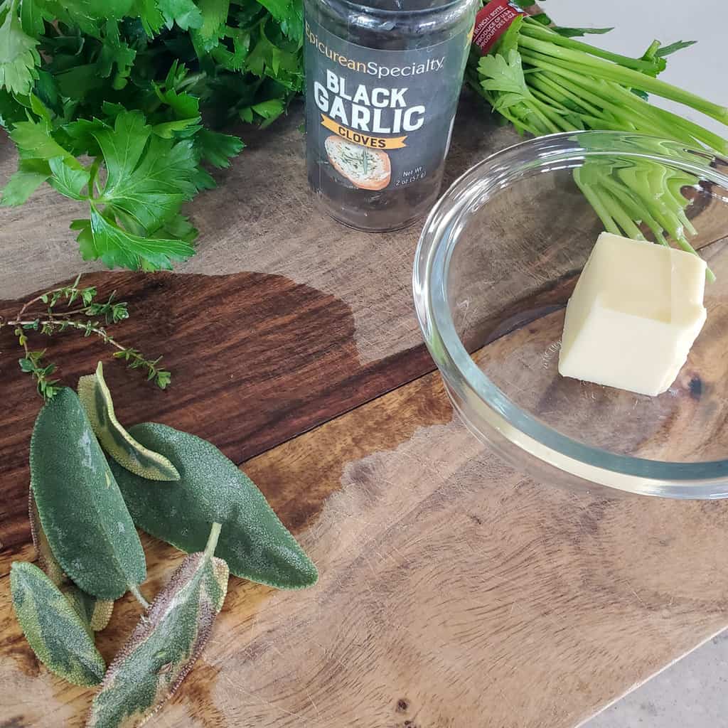 Sage, butter, parsley and black garlic on a cutting board.