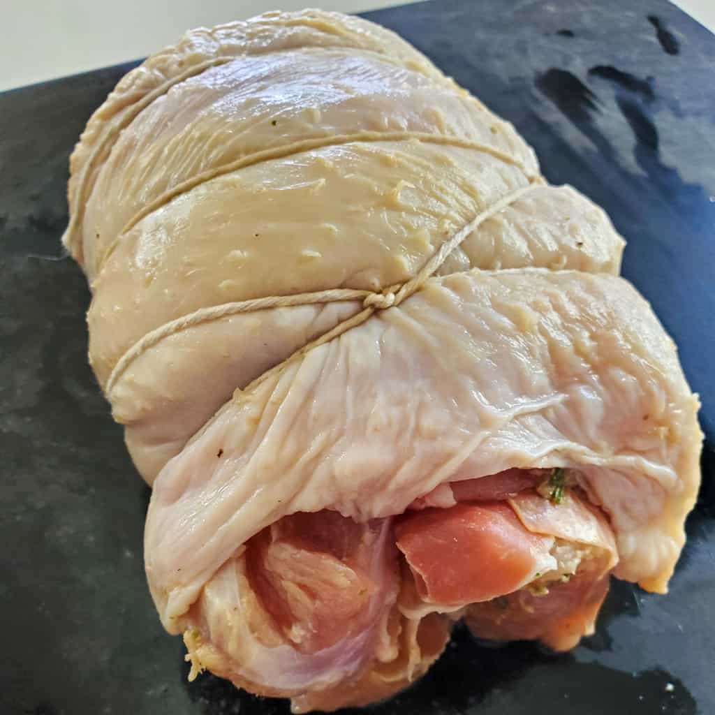 Herb stuffed turkey breast with herbs, black garlic, and prosciutto, tied with twine.