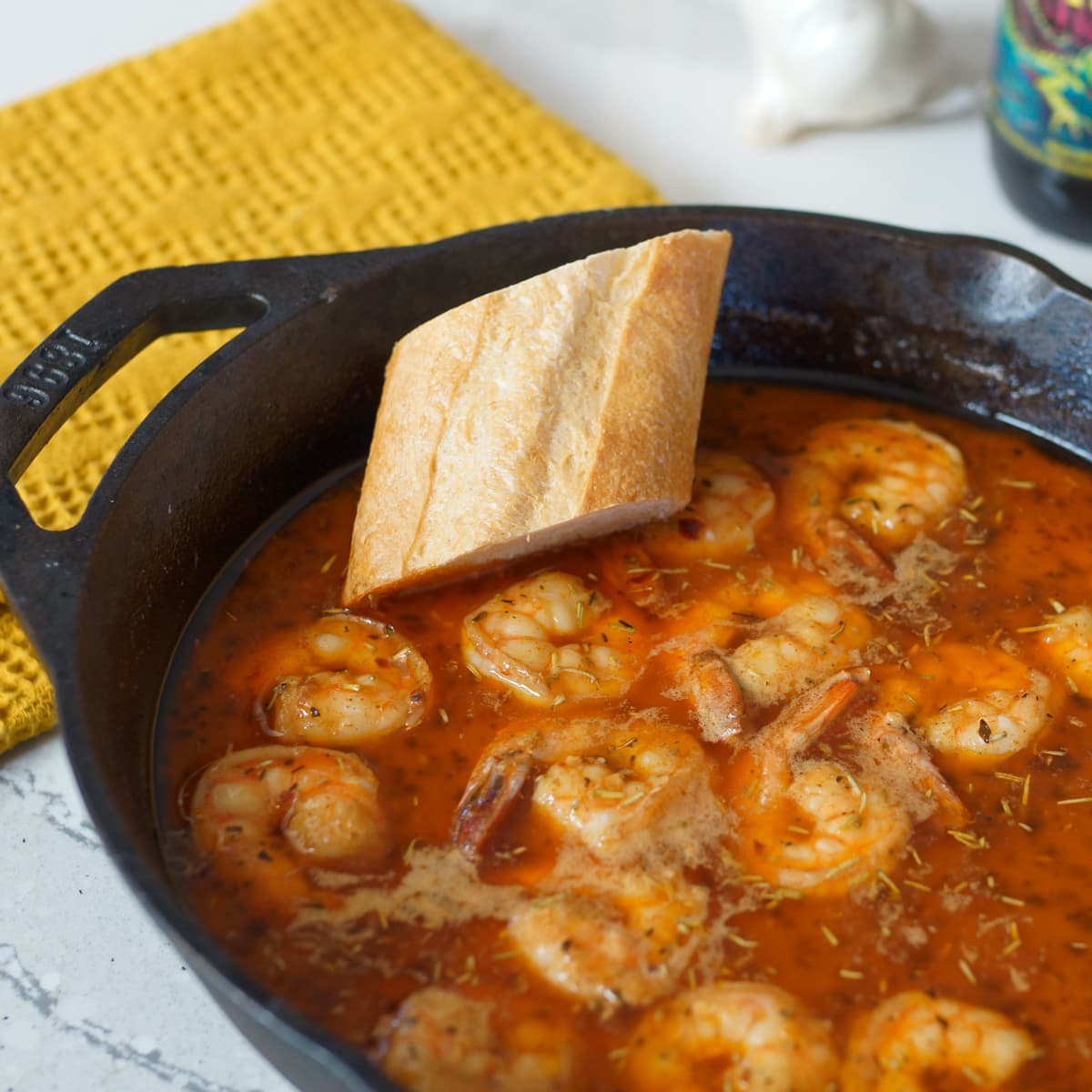 Cast iron Creole style shrimp with a slice of baguette.