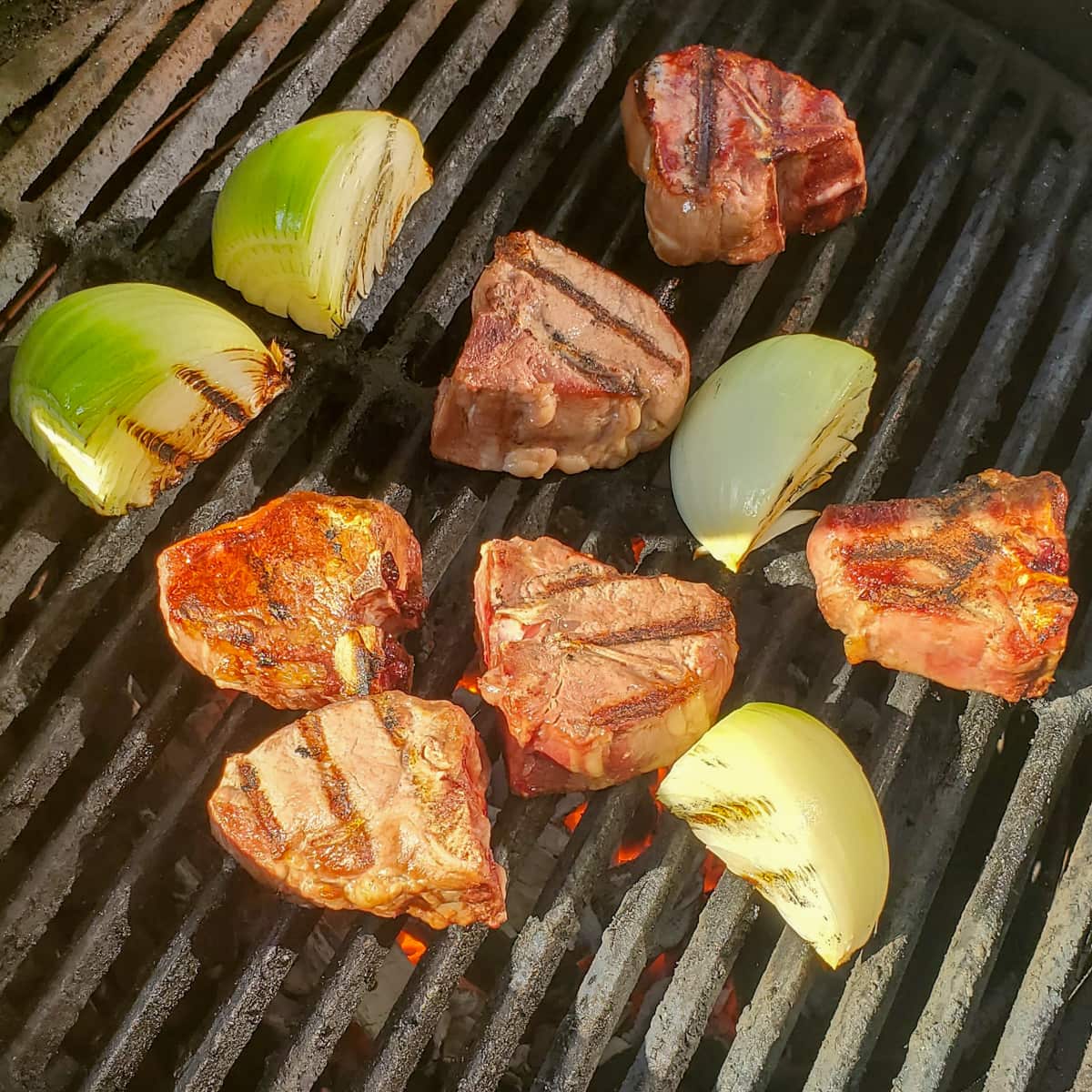 Onions and lamb chops cooking on a grill.